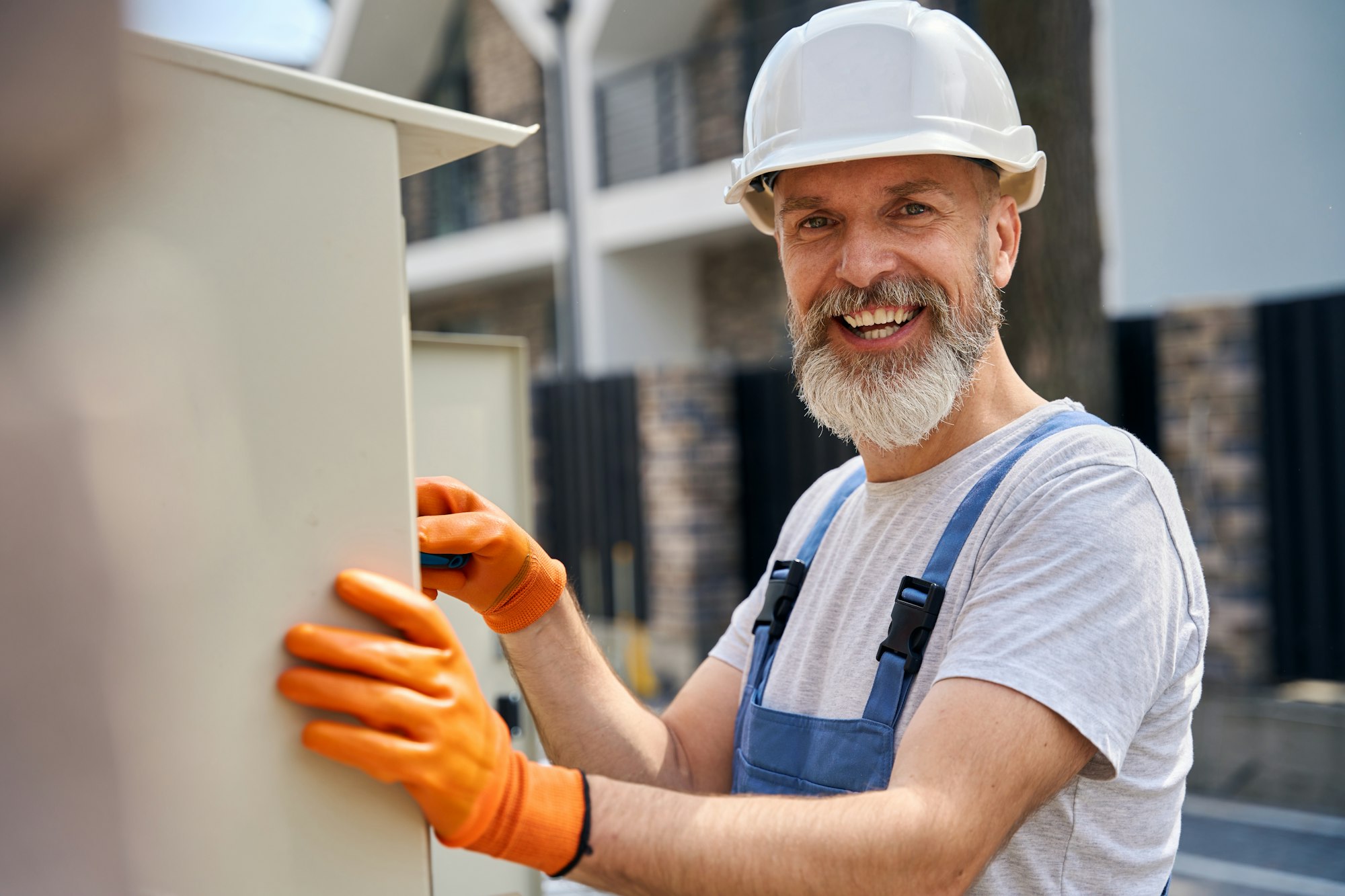 Joyful electrician mounting electric switchboard outdoors